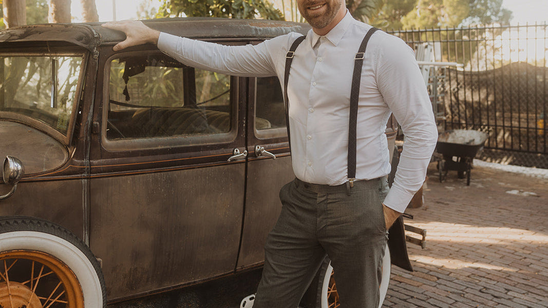 Man wearing suspenders and posing next to vintage car