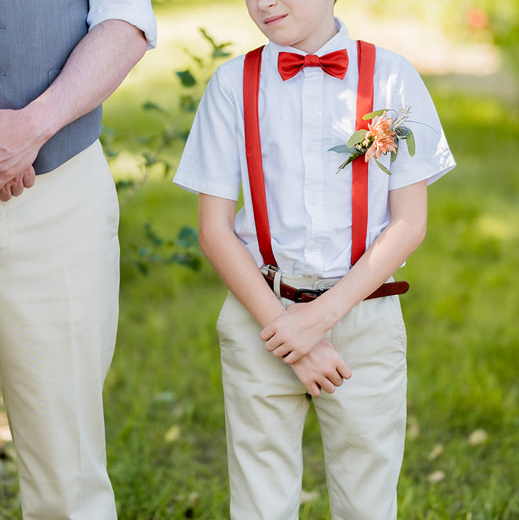 photo of boy wearing matching solid colored bow tie and suspenders at a wedding