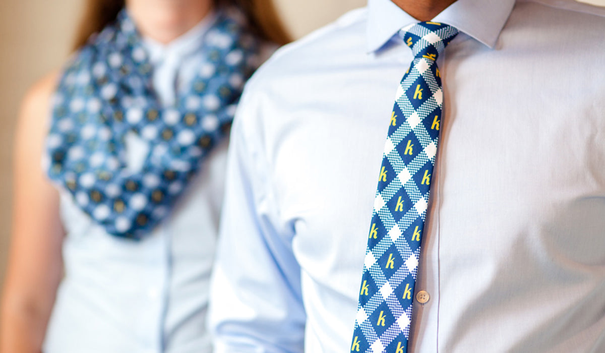 man wearing logo necktie in foreground and woman wearing matching logo scarf in background